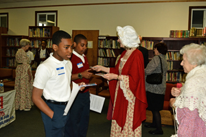 Volunteers from Women for Greater Philadelphia dressed in period costumes hand out a pocket guide to the constitution to the participating students of Holy Cross School.