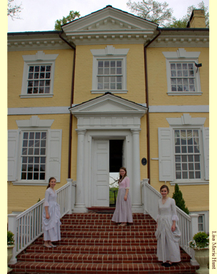 Three young women in costume on thesteps leading to the grand entrance of Laurel Hill Mansion